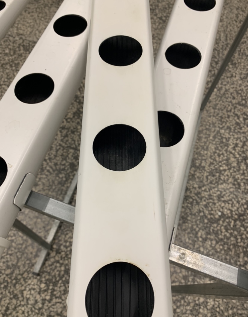 1 metro Perfil Perforado de 80 mm con Tapón - Segunda mano Tubes de cultivo hidropónico brancos com orifícios pretos em suporte metálico.