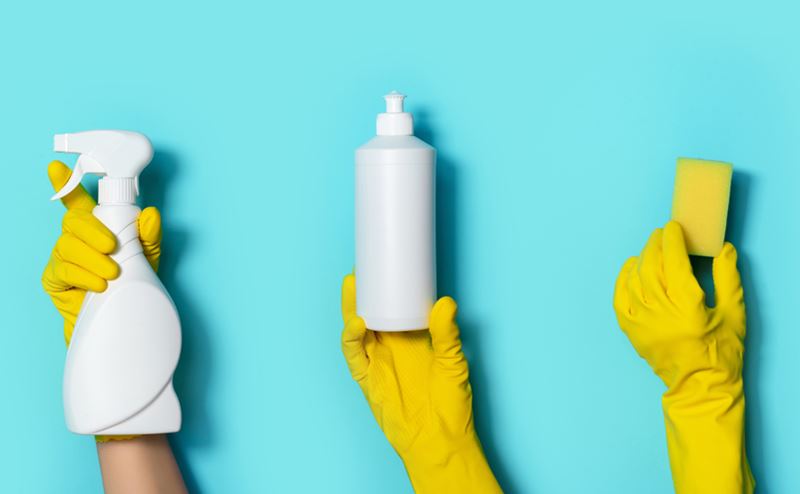 Mãos com luvas amarelas segurando frascos brancos e esponja amarela