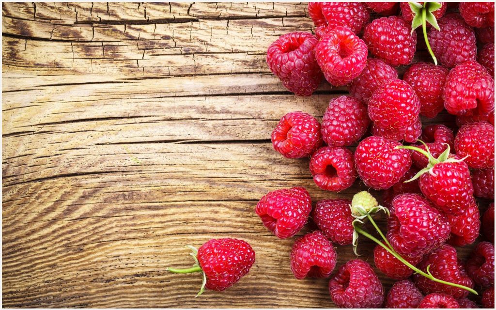Framboesas vermelhas frescas sobre madeira clara com textura natural