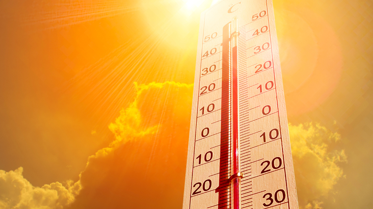 Termómetro vertical com escala de -30 a 50 graus sob sol brilhante e céu laranja