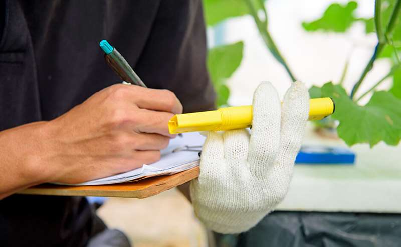 Pessoa escrevendo em bloco de notas com marcador amarelo e caneta azul, usando luva branca