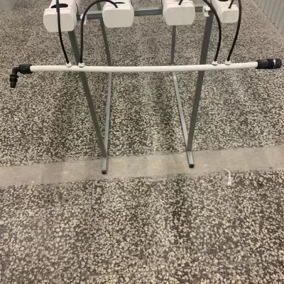 Estrutura metálica com tubo branco e conectores pretos sobre chão de pedra