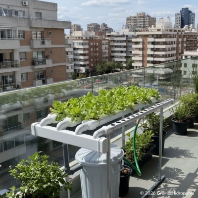 Sistema hidropónico con plantas en un balcón urbano con barandilla de vidrio.