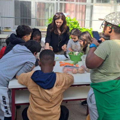 Crianças e mulher numa cozinha em torno de uma mesa com legumes.