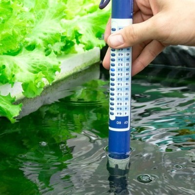 Medidor azul e branco na água de um tanque com plantações verdes ao fundo
