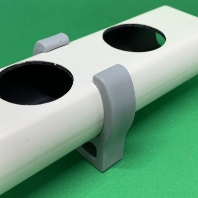 Suporte branco cilíndrico com orifícios e presilhas cinzentas sobre fundo verde