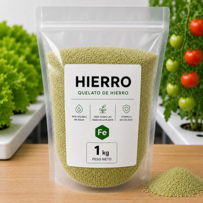 Bolsa transparente con quelato de hierro en gránulos verdes y etiqueta con texto informativo colocada sobre una mesa de madera, con plantas y tomates en el fondo.