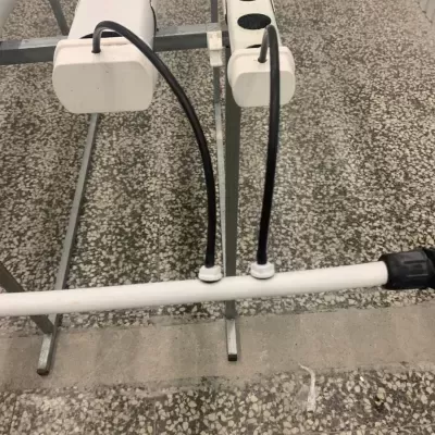 Suporte de metal com tubos pretos flexíveis e barra branca sobre chão de azulejo.