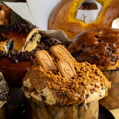 Panetone com cobertura de biscoito Lotus e pedaços de chocolate numa mesa com outros panetones