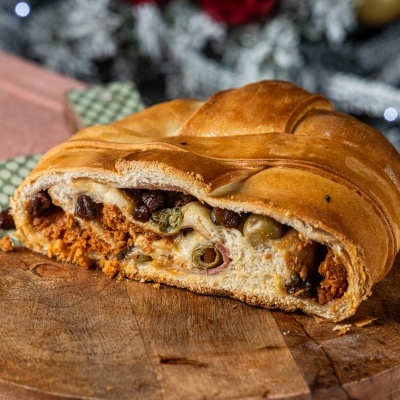 Pão recheado com chouriço, azeitonas e passas sobre base de madeira