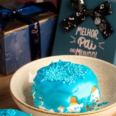 Bolos decorados com cobertura azul e pérolas azuis em tigelas com caixas de presente ao fundo.