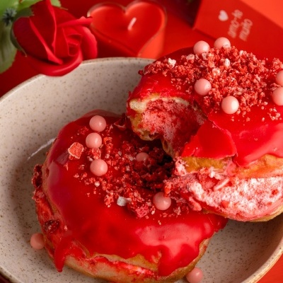 Dois donuts vermelhos num prato branco com decoração romântica ao fundo