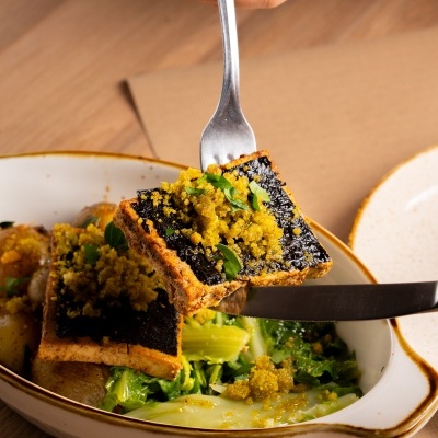 Prato com tofu grelhado e legumes verdes numa tigela branca sobre mesa de madeira