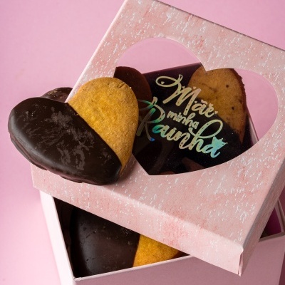 Bolachas em forma de coração parcialmente cobertas de chocolate em caixa rosa com tampa e janela em coração