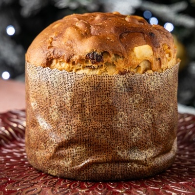 Panetone com frutos cristalizados em papel decorativo castanho, sobre prato vermelho texturizado.