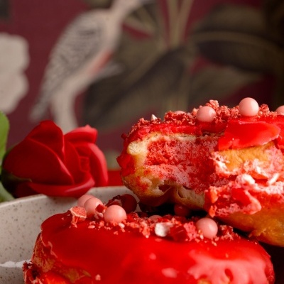 Rosquilhas vermelhas com granulado e decoração, em taça de cerâmica junto a rosa vermelha