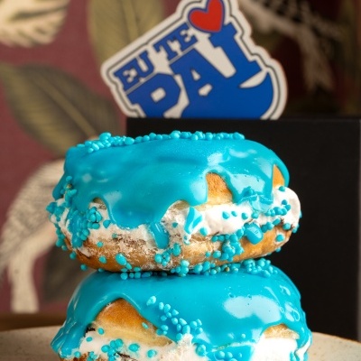 Dois donuts com glacê azul e confeitos azuis empilhados em prato com fundo de folhas e pássaros.