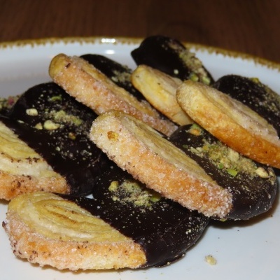 Bolachas palmiers com chocolate e pistachos no prato branco.