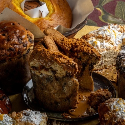 Vários tipos de bolos e pães doces tradicionais com cobertura e recheios variados em mesa.