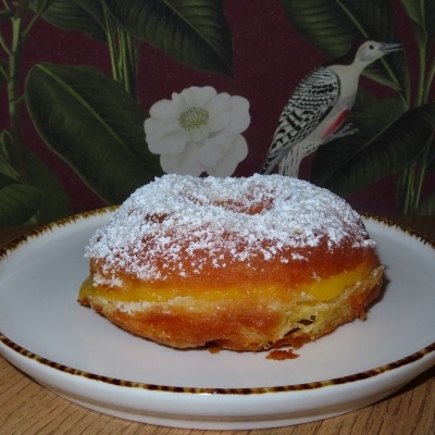 Doce rosquinha com açúcar em pó no prato branco sobre mesa de madeira, com fundo floral e pássaro