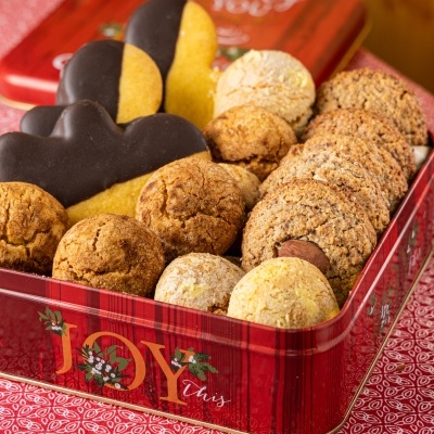 Caixa metálica vermelha com biscoitos variados incluindo biscoitos meio cobertos de chocolate escuro, redondos e granulados sobre pano vermelho estampado.