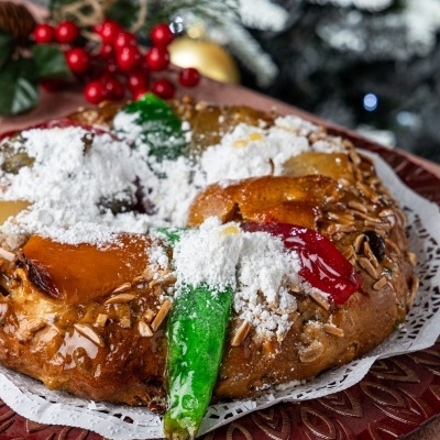 Bolo-rei com frutas cristalizadas e amêndoas num prato vermelho com decoração natalícia ao fundo
