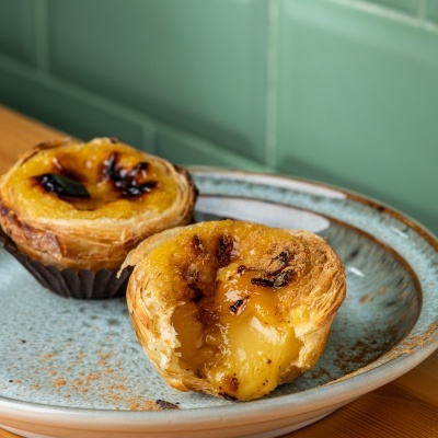 Dois pastéis de nata em placa azul sobre mesa clara