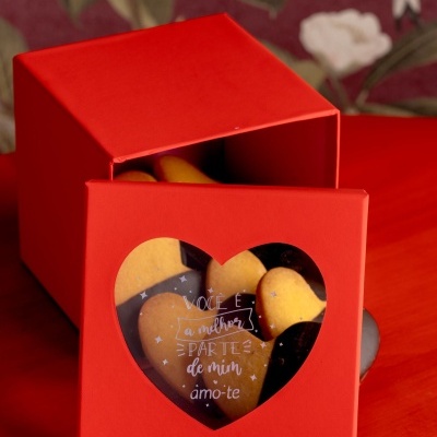 Caixa vermelha com biscoitos em forma de coração e janela com texto em português.