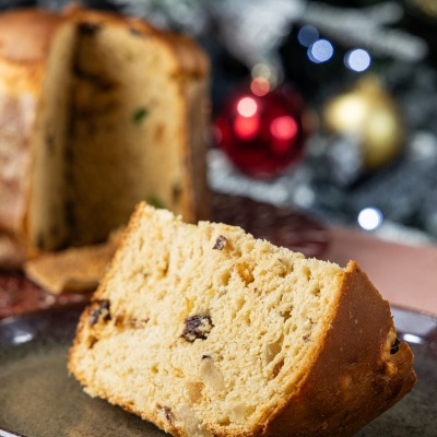 Fatias de panetone com passas em prato castanho, fundo com decoração natalícia desfocada