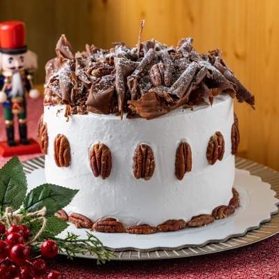 Bolo decorado com chantilly branco, pecãs e lascas de chocolate em ambiente festivo