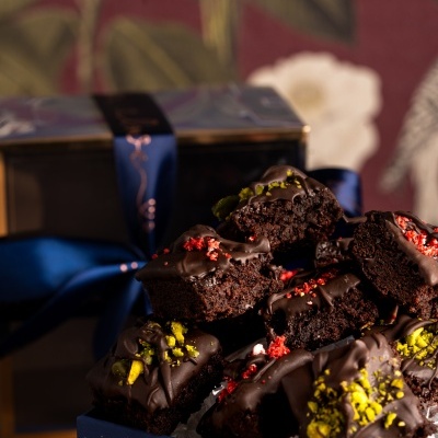 Bolos quadrados cobertos de chocolate preto com toppings coloridos numa caixa azul