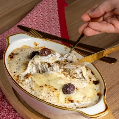 Prato cerâmico com lasanha cremosa e azeitonas em mesa de madeira com guardanapo vermelho