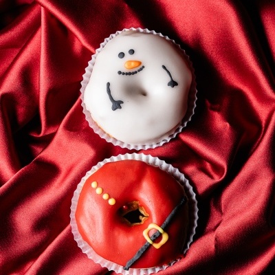 Dois donuts decorados de Natal, um como boneco de neve e outro como cinto de Papai Noel sobre tecido vermelho.