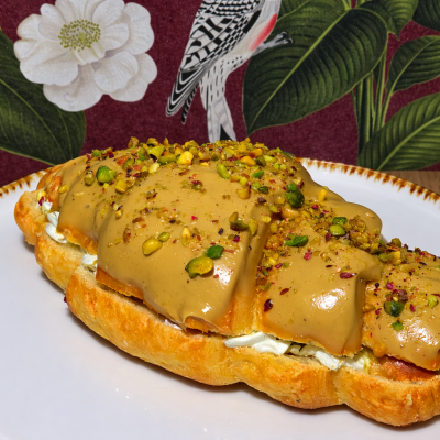 Croissant aberto com creme caramelizado e pistachio num prato branco sobre mesa de madeira e fundo floral