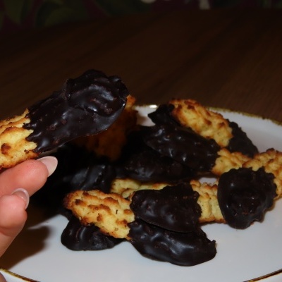Biscoitos cobertos parcialmente por chocolate em prato branco sobre mesa de madeira.