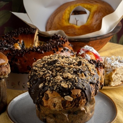 Bolos tradicionais, incluindo panetone com cobertura de chocolate e nozes, sobre mesa com toalha amarela
