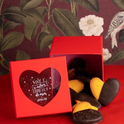 Caixa vermelha com biscoitos em forma de coração cobertos parcialmente de chocolate em mesa vermelha