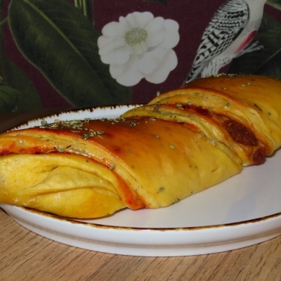 Pão recheado dourado num prato branco sobre mesa de madeira com fundo floral