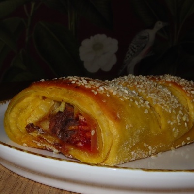 Rolo de massa folhada amarela com sementes e recheio de carne e batata