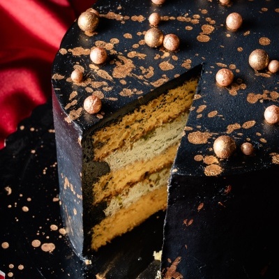 Bolo preto com detalhes dourados e esferas em cima, fatia cortada mostrando camadas interiores