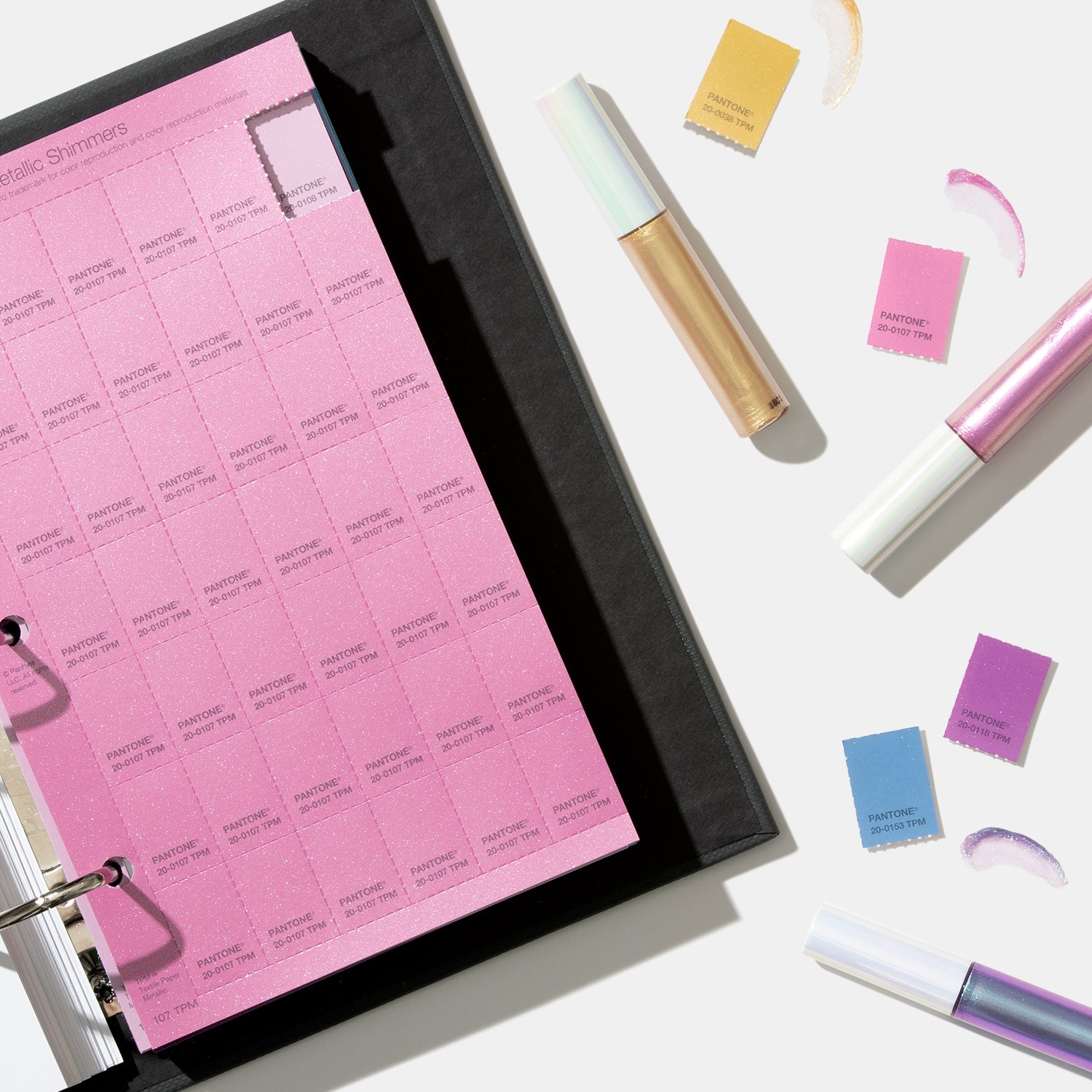 Folha Pantone rosa num fichário com maquilhagem e cartões Pantone coloridos numa superfície branca