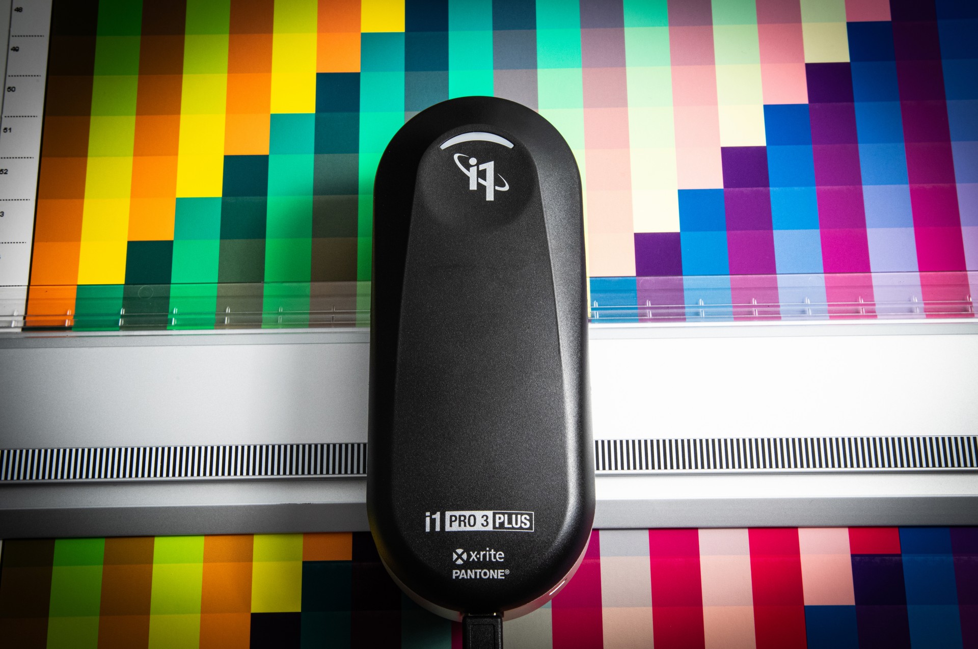 i1 Publish Pro 3 Plus Dispositivo de calibração de cor preto i1 PRO 3 PLUS sobre superfície branca com fundo colorido