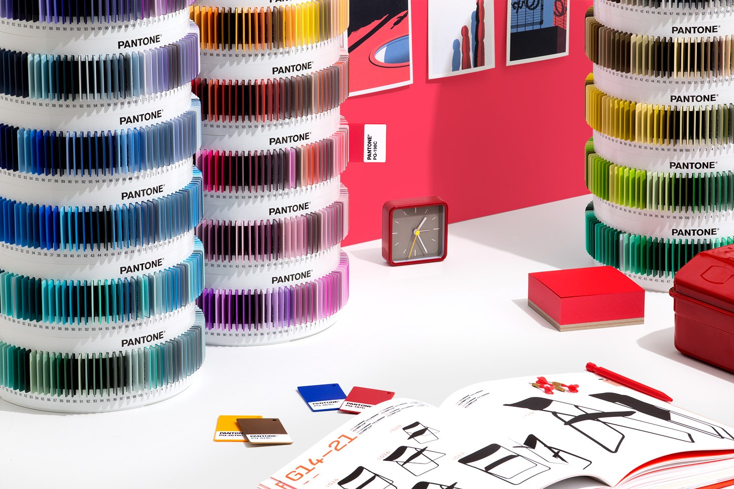 Pantone Plus Plastic Standard Chips Collection Conjuntos de amostras de cores Pantone em discos rotativos transparentes sobre mesa branca com relógio, livros vermelhos e catálogo de móveis.