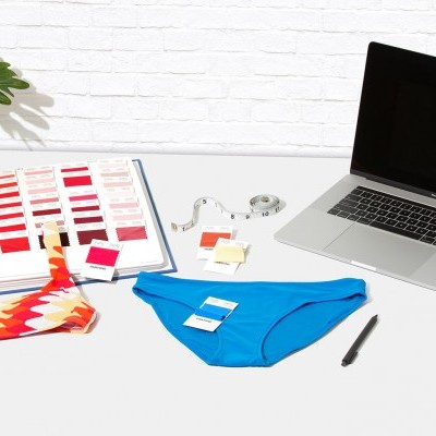 dois fatos de banho coloridos, portátil, fita métrica e amostras de cores numa mesa branca