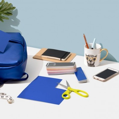 Mochila azul e material escolar sobre mesa branca com fundo azul claro