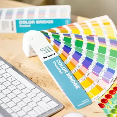 Cartela de cores Pantone Color Bridge Uncoated sobre mesa de madeira com teclado branco