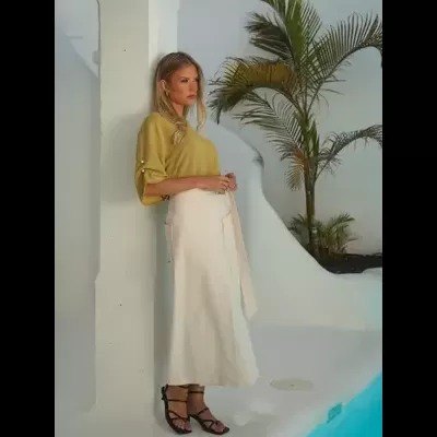 Mulher com camisola verde-lima de mangas 3/4, saia branca comprida e sandálias pretas junto a piscina