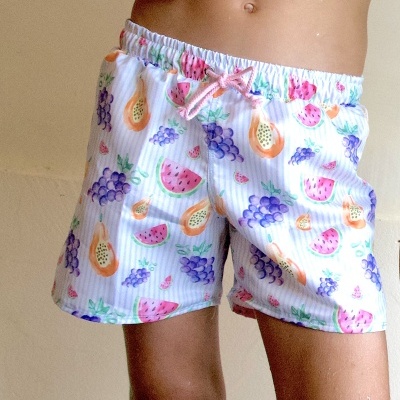 Calções de criança com padrão de frutas coloridas e cordão rosa na cintura.