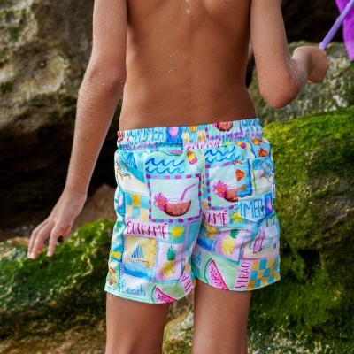 Calções de banho coloridos com padrões de praia usados por criança numa praia com rochas e areia