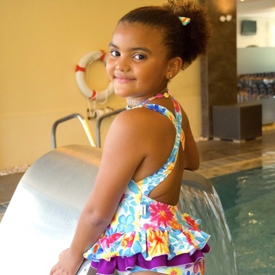 Fato de banho infantil floral colorido com babados roxos junto a piscina interior